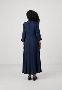 Tumši zilas krāsas, garām piedurknēm, kleita ar apkakli, plūstoša A-silueta un līdz celim garuma. Gluda auduma virsma bez redzamām rakstām.