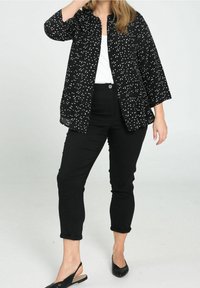 Chaqueta negra con lunares blancos, con botones en la parte delantera, mangas de tres cuartos, usada sobre una parte superior blanca, combinada con pantalones negros y bailarinas.