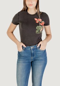 T-shirt in cotone nero con stampa floreale rossa e verde sul lato sinistro, abbinata a jeans a vita alta in denim blu.