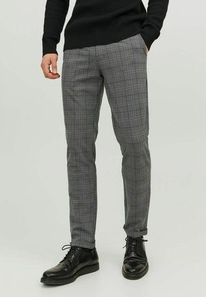 Pantaloni grigi a quadri con vestibilità sartoriale, caratterizzati da una vita piatta, tasche laterali e dettagli sottili in tonalità più scure. Indossati con scarpe nere.