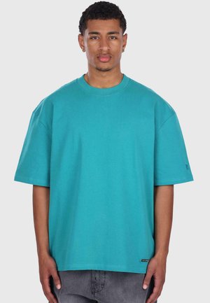 Tricou oversized din bumbac turcoaz, cu mâneci scurte, decolteu rotund și un eticheta mică la tiv. Textură netedă, cu o croială lejeră.