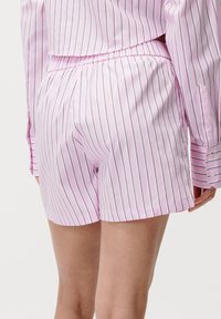 Rosa stripete shorts med elastisk midje og sidelommer. Stoffet ser glatt ut med vertikale linjer i mørkere farger.