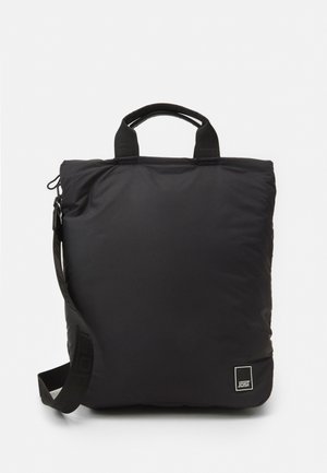 Sac fourre-tout rembourré noir avec double poignée supérieure, bandoulière réglable et patch logo à l'avant. Présente une texture lisse et une forme rectangulaire.