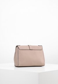 Borsa rettangolare beige con una patta testurizzata e una tracolla magnetica, esposta su un piedistallo bianco su uno sfondo semplice.