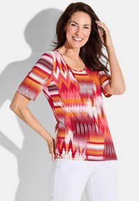 Multi-kleurige korte mouwen top in rood, oranje en roze met een abstract zigzagpatroon; heeft een ronde halslijn en een aansluitend ontwerp.