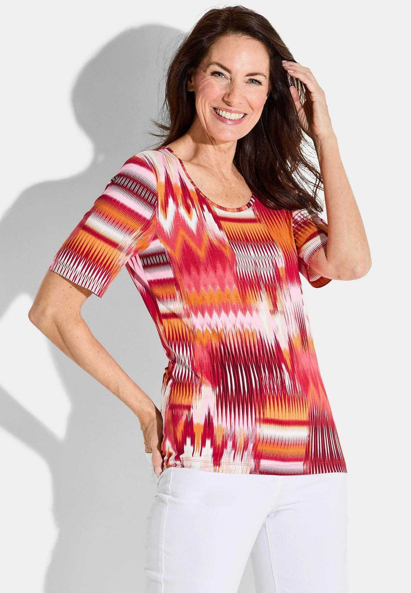 Multi-kleurige korte mouwen top in rood, oranje en roze met een abstract zigzagpatroon; heeft een ronde halslijn en een aansluitend ontwerp.