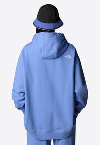 Haut à capuche bleu clair avec une coupe décontractée, un tissu durable et une poche kangourou à l'avant. L'arrière présente un petit logo blanc et des poignets côtelés.