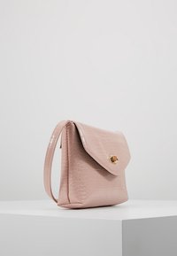 Pale pink, faux crocodile leather handbag with a folded flap, gold-tone hardware, and a single shoulder strap, featuring a smooth, glossy texture.