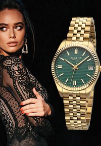 Montre dorée avec un cadran texturé vert, des index argentés et une fonction date. Présente un bracelet à maillons et une lunette striée pour un détail supplémentaire.