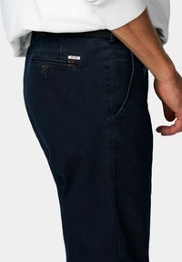 Pantalons en denim bleu marine avec une poche latérale et un patch arrière affichant le nom de la marque. Doté d'une fermeture à bouton et d'une texture lisse.