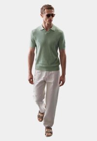 Pletené mátově zelené polo tričko s krátkými rukávy, spárované s volnějšími světle béžovými kalhotami a hnědými pantofli.