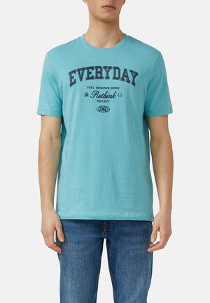 Homme portant un t-shirt bleu clair avec le texte noir "EVERYDAY" et des mots plus petits "Feel Observe Grow Rethink Reflect", associé à un jean bleu.