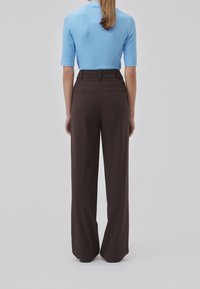 Un top azzurro chiaro a maniche corte si abbina a pantaloni marroni a vita alta con gamba larga. I pantaloni presentano due tasche posteriori e una texture liscia.