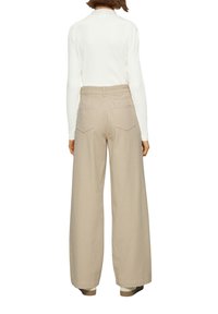 Pantalons larges beiges à taille haute, en coton. Dotés de deux poches arrière et d'une texture lisse. Associés à un haut blanc à côtes.