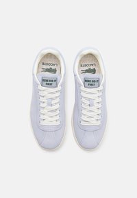 Zapatillas de ante de color lila claro con cordones blancos, que cuentan con una etiqueta verde que dice "RENE LO HIZO PRIMERO" y una plantilla estampada.