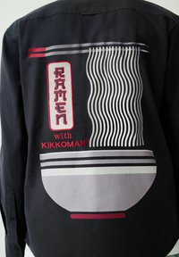 Čierne tričko s grafikou misy ramenu, červenými a sivými akcentmi, štýlizovanými rezancami a textom "RAMEN s KIKKOMAN".