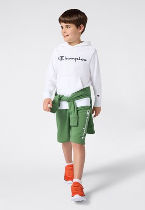 Felpa bianca con logo "Champion", pantaloncini verdi annodati in vita e scarpe da ginnastica arancioni. Caratterizzata da tessuto morbido e vestibilità comoda.