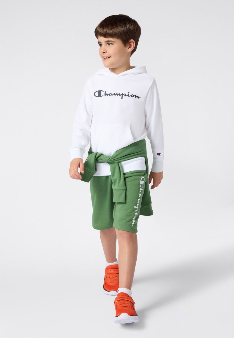 Felpa bianca con logo "Champion", pantaloncini verdi annodati in vita e scarpe da ginnastica arancioni. Caratterizzata da tessuto morbido e vestibilità comoda.