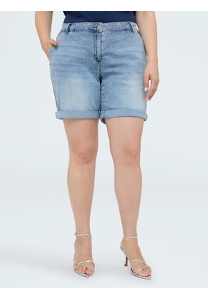 Vrouw die lichtblauwe denimshorts draagt met opgerolde zomen en kleine versieringen, gecombineerd met zilveren sandalen met hoge hakken.