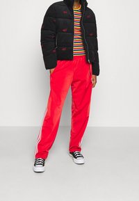 Kurtka puchowa z czarnego sztruksu z czerwonymi akcentami, wielokolorowa koszula w paski oraz czerwone satynowe spodnie dresowe z białymi paskami po bokach. Czarne sneakersy.