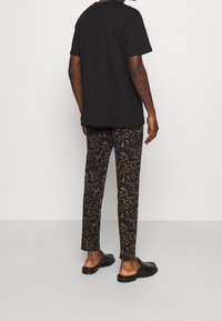 Czarna bawełniana koszulka z luźnym krojem, w połączeniu z czarnymi i brązowymi spodniami w wzory. Całość dopełniają czarne buty wsuwane.