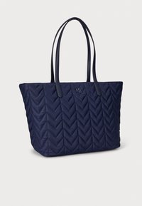 Granatowa pikowana torba na ramię z wzorem w jodełkę, wyposażona w dwa długie uchwyty i wypukłe logo na przedniej stronie. Zewnętrzna powierzchnia z tkaniny o fakturze.
