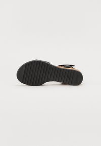 Black sandal with textured rubber sole, featuring a slightly raised heel, adjustable strap, and cork detailing on the footbed.