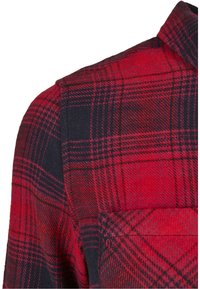 Tissu à carreaux rouges et noirs montrant les détails de l'épaule, du col et de la poche poitrine supérieure d'une chemise.