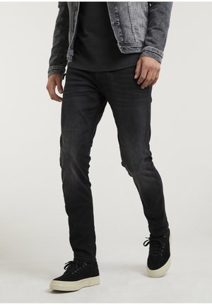 Mörk tvättade denimjeans med smal passform, tillsammans med en svart T-shirt och en grå denimjacka. Har svarta mockaskor med vita sulor.