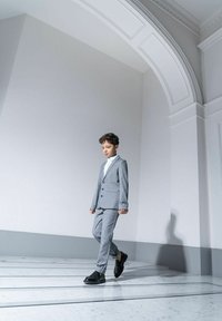 Szary garnitur z klapami w kształcie notcha, czarnymi guzikami i dopasowanymi spodniami. W parze z białą koszulą i czarnymi butami. Gładka tekstura, dopasowany krój.