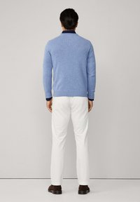 Světle modrý pletený svetr s kulatým výstřihem, kontrastním námořnicky modrým límcem, v kombinaci s bílými kalhotami a tmavě hnědými botami. Zadní pohled.