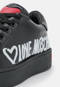Svart lädersneaker med vit "LOVE MOSCHINO" text, röd hjärtaccent på tungan och texturerad svart sula.