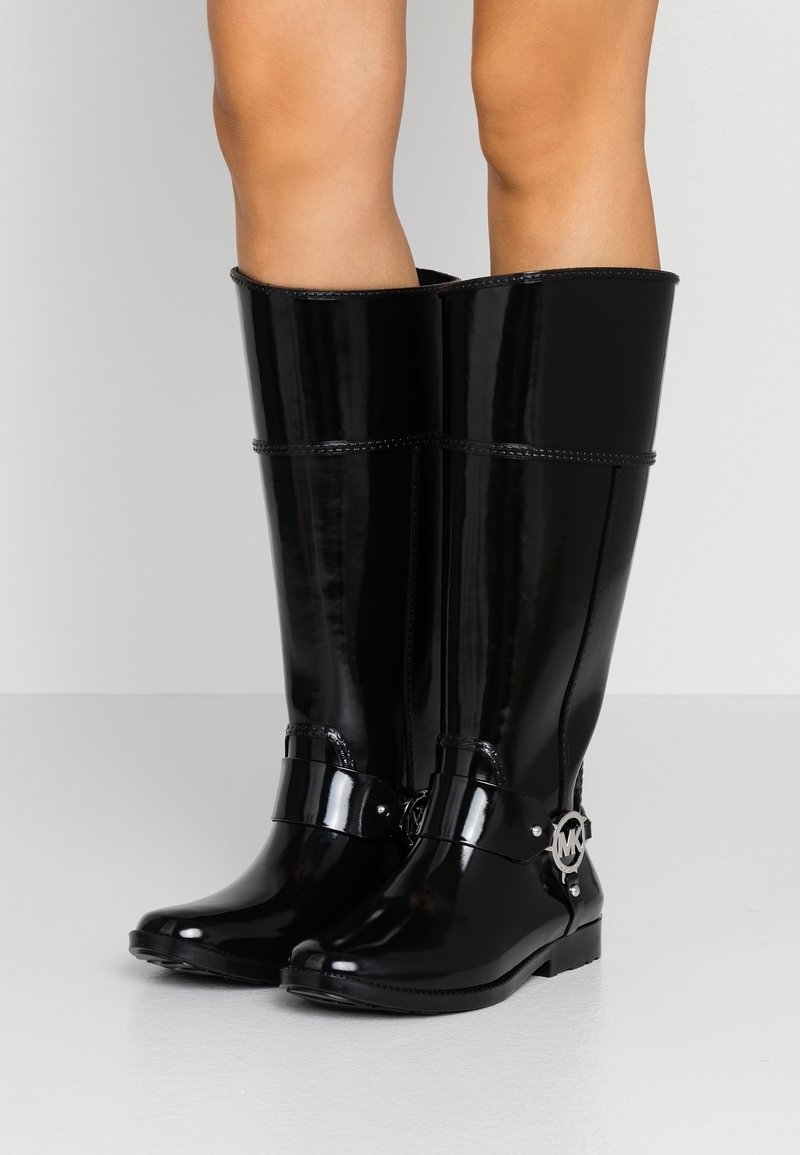 Czarne, lakierowane, wysokie botki do kolan o gładkim wykończeniu, z paskiem z metalowymi elementami i okrągłym detalem z logo po bokach.