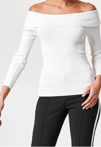 Haut blanc à épaules dénudées en tissu côtelé avec manches longues, doté d'une texture lisse et d'une coupe ajustée, accompagné d'un pantalon noir avec des bandes blanches sur les côtés.