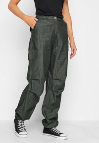Spodnie cargo w ciemnozielonym kolorze, charakteryzujące się luźnym krojem, wieloma kieszeniami bocznymi oraz zapięciem na guzik, w połączeniu z czarnymi sneakersami za kostkę.