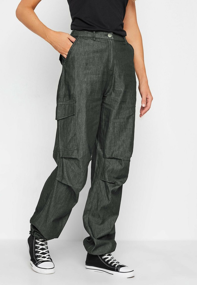 Spodnie cargo w ciemnozielonym kolorze, charakteryzujące się luźnym krojem, wieloma kieszeniami bocznymi oraz zapięciem na guzik, w połączeniu z czarnymi sneakersami za kostkę.