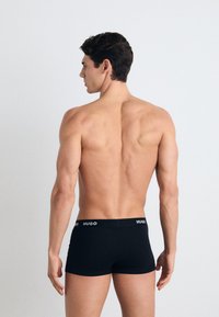 Boxers negros hechos de una tela suave, con una cinturilla marcada que dice "HUGO" en blanco, exhibidos desde la parte posterior con un fondo neutro.
