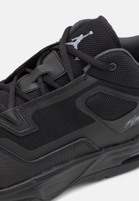 Svart idrottssko med nät- och läderpaneler, svarta snören och en vit Jumpman-logotyp på tungan.