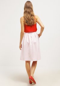 Top rosso con spalline sottili abbinato a una gonna plissettata rosa. La gonna presenta una cerniera posteriore, e il modello indossa scarpe rosse con dettagli ritagliati.