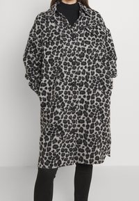 Oversized Mantel mit Leopardenmuster in Grau und Schwarz, ausgestattet mit einem Knopfverschluss, zwei Brusttaschen und einem Kragen, aus einem weichen, strukturierten Stoff gefertigt.