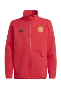 Giacca rossa con zip in pile, con colletto alto, logo Adidas nero e stemma del Manchester United in oro sul lato sinistro del petto.