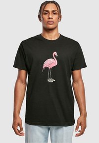 Juodas medvilninis marškinėliai su rožiniu flamingo grafika ir languotais batais, trumpomis rankovėmis ir apvaliu kaklu. Patogi ir laisva fasono dizainas.