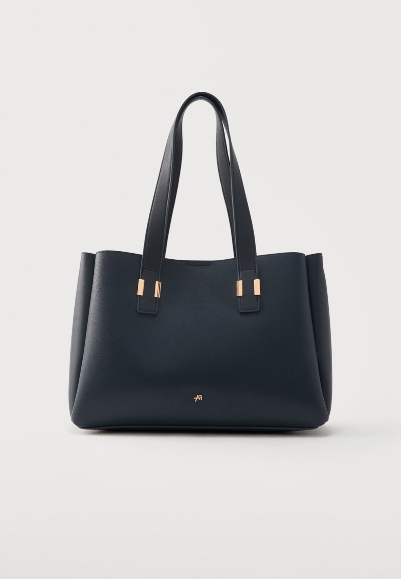 Sac cabas en cuir noir avec double poignée et accents métalliques dorés, présenté sur fond gris clair.