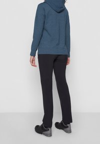 Blå mönstrad hoodie med dragsko i huvan, kombinerad med svarta byxor. Plagget har en avslappnad passform och slitstarkt tyg. Svarta sportiga skor.