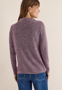 Fioletowy, teksturowany sweter z długim rękawem o subtelnej wzorze heather, okrągłym dekolcie i luźnym kroju, zestawiony z jasnoniebieskimi dżinsami.