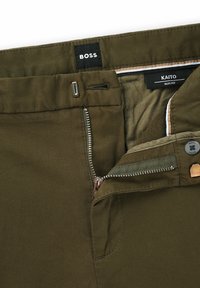 Olivgröna slim-fit byxor med dragkedja, flera fickor och BOSS-logotyp. Har en slät, texturerad tyg och kontrasterande innerfoder.