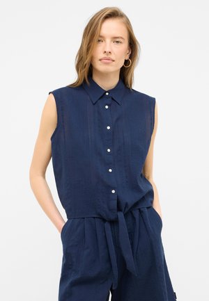 Maglietta senza maniche blu navy con chiusura a bottoni, colletto e strisce testurizzate. Presenta un dettaglio con vita annodata e tasche laterali.