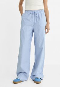 Pantalons larges à rayures bleues et blanches avec une taille élastique et un cordon de serrage, fabriqués en tissu léger, associés à des chaussures bleues.