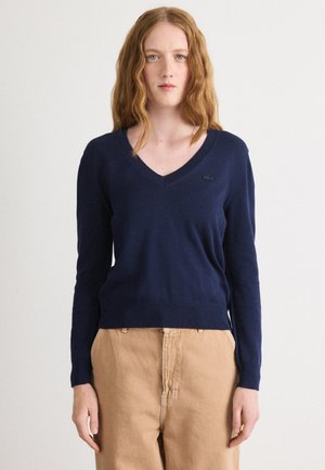 Maglione a V blu navy realizzato in tessuto leggero e morbido. Presenta maniche lunghe, polsini e orlo a coste, e un piccolo logo di accento.