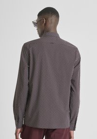 Langemouwen shirt in donker maroon met een geometrisch wit patroon. Voorzien van een kraag en knoopmanchetten, gemaakt van lichtgewicht stof.